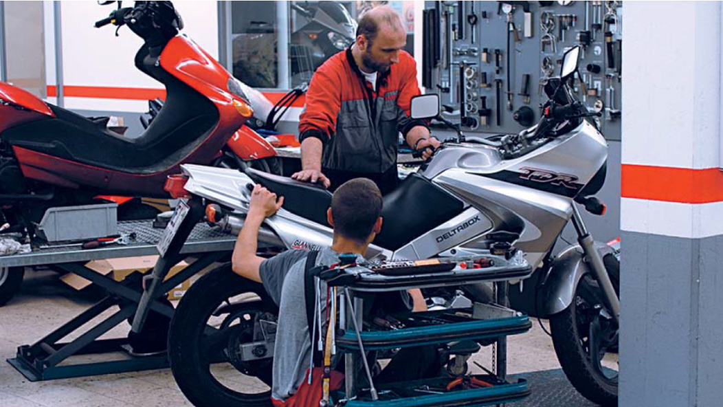 İki kişinin bir motosiklet üzerinde çalıştığı bir atölyenin fotoğrafı.
