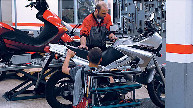 Otomobil Tamirhanesi İki kişinin bir motosiklet üzerinde çalıştığı bir atölyenin fotoğrafı.